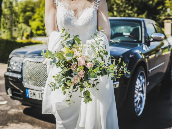 pexels-photo-2318049-2318049 Bride in white gown holding a bouquet near a luxury car, symbolizing elegance and romance.